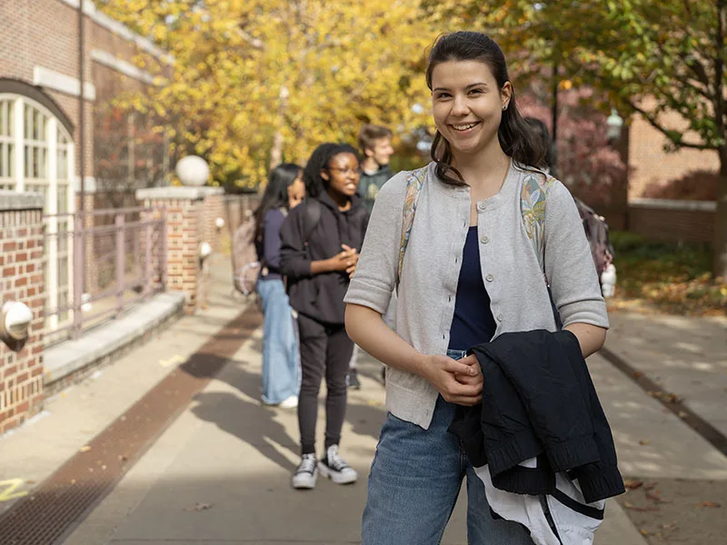 Smiling student in campus courtyard with group of students in the background.