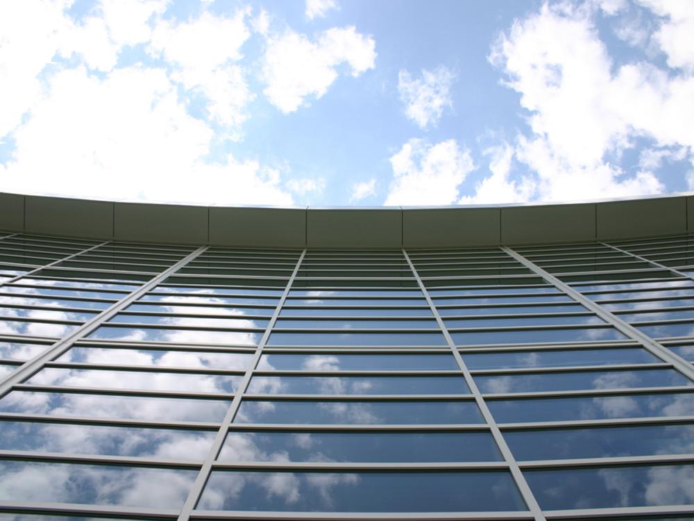 A photo of windows in the Penn State Business Building looking up toward a blue sky with white clouds.