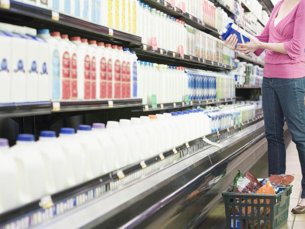 A person holds a carton of milk in a supermarket dairy aisle