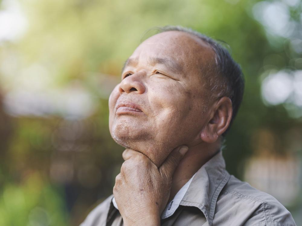 An elderly man holds his sore throat.
