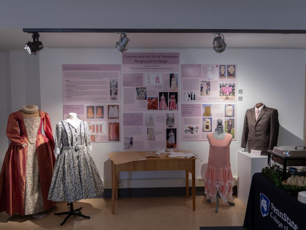 Three dresses and a men's suit displayed on mannequins as part of an exhibition.