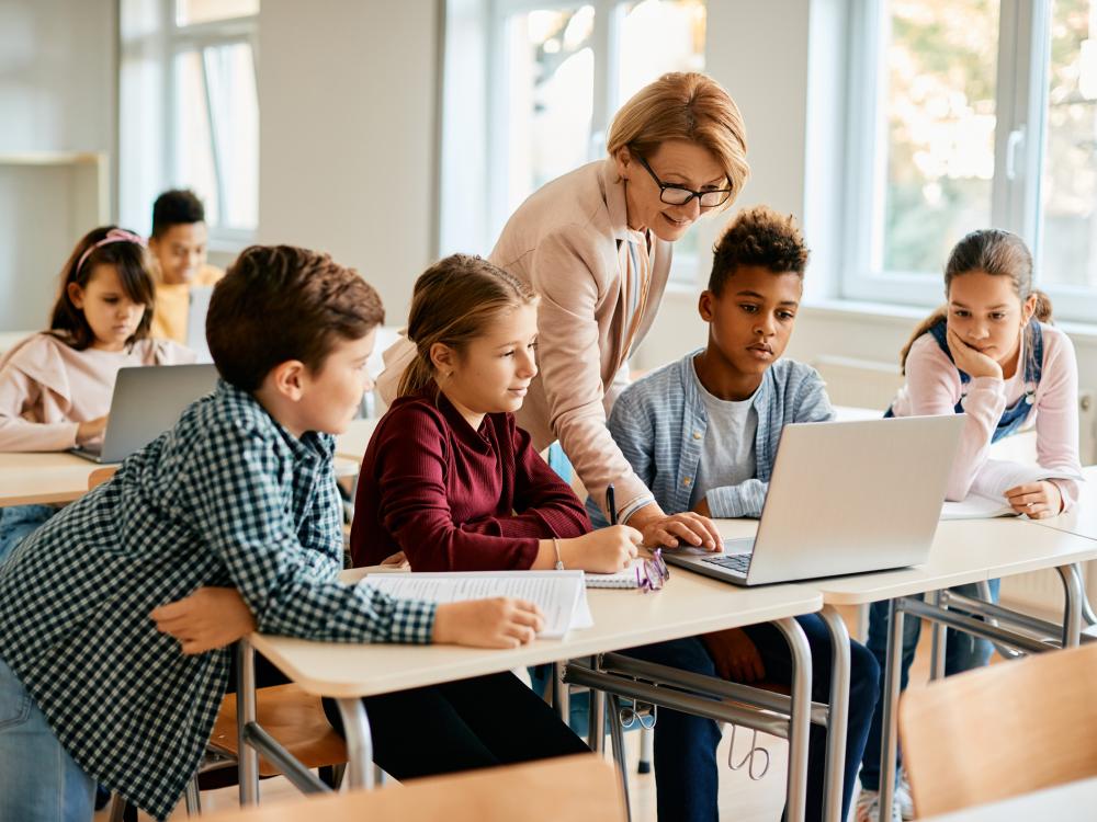 Elementary teacher and students using a laptop during class.