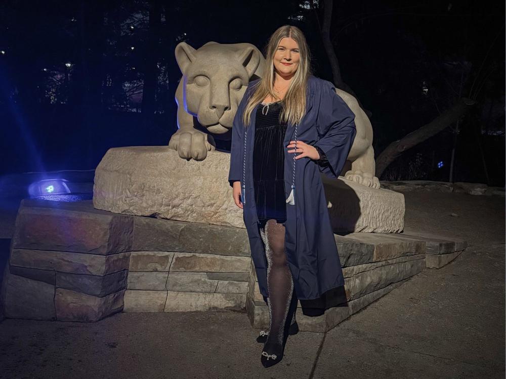 Jillian Lesikar stands in front of the Nittany Lion Shrine in her graduation gown in the dark.