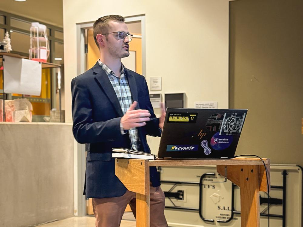 Kieron Cook standing at a podium with an open laptop in front of him