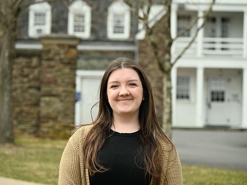 A female student stands outside in front of historic Hayfield House.