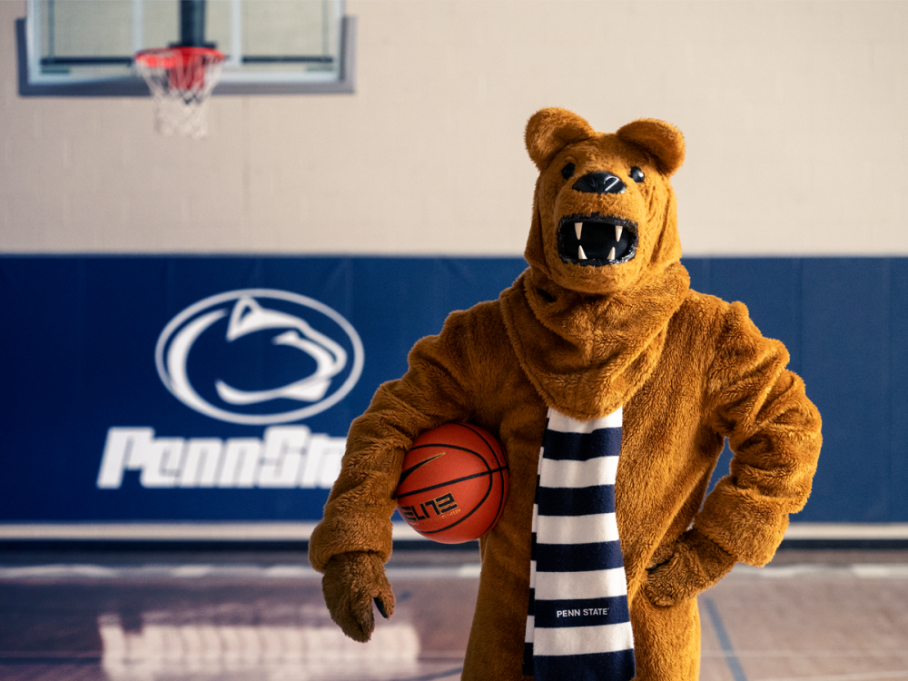 The Nittany Lion mascot stands on the court with a basketbal at their waist.